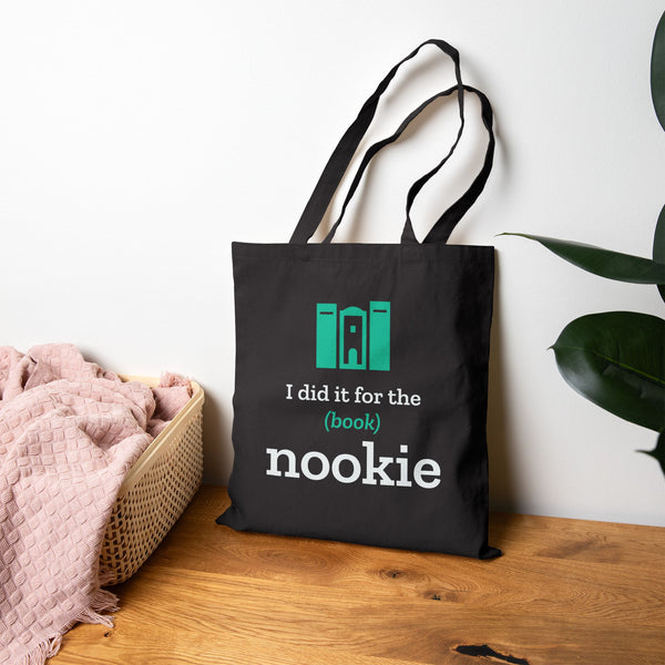 Black book lover tote bag propped on a wood floor beside a bed