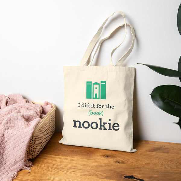 Natural book lover tote bag propped on a wood floor beside a bed